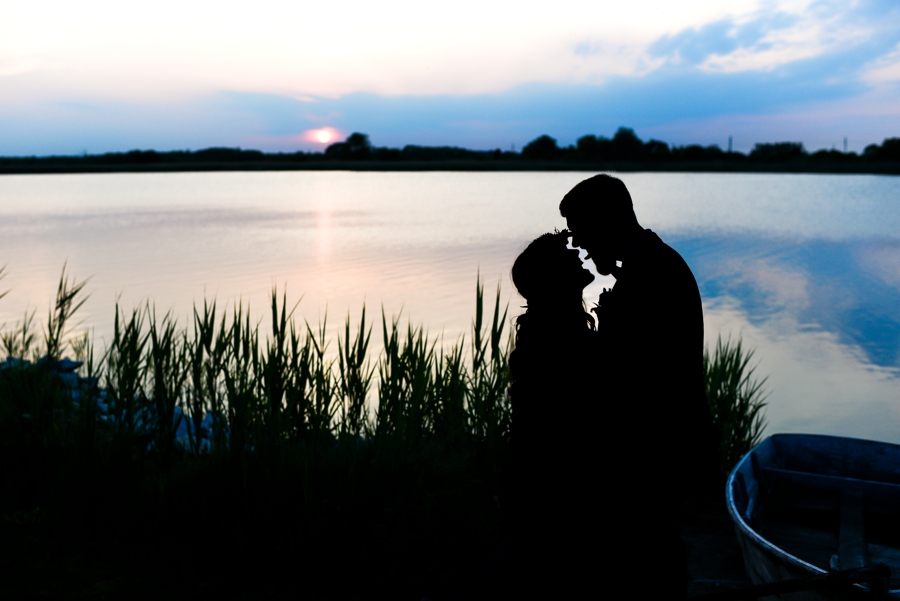 A silhouette of a bride and groom kissing by the river at sunset.